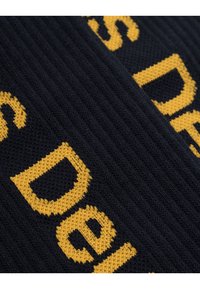 Tessuto a maglia nero con un audace motivo testuale giallo brillante. Presenta una texture a coste, enfatizzando il design e il contrasto del carattere.
