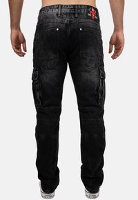 Black denim cargo pants with a relaxed fit, visible stitching details, multiple pockets, and contrasting red accents on the waistband.