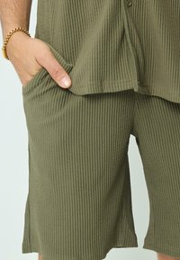 Shorts en tissu côtelé vert avec poches latérales, une coupe décontractée et un ourlet qui descend légèrement en dessous du genou.