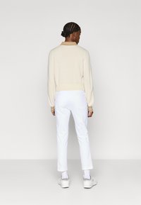 Kremgenser med en beige krage, hvite bukser og hvite sneakers. Genseren har tettsittende mansjetter og en glatt tekstur, mens buksene er rettkuttet.