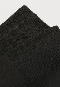 Chaussettes noires sans couture avec une texture côtelée, fabriquées en matériau lisse et à la forme uniforme, conçues pour le confort et l'ajustement.