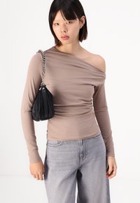 Bluză cu mâneci lungi, off-shoulder, din țesătură bej cu detalii pliate, asociată cu blugi gri deschis cu talie înaltă și o poșetă mică neagră cu curea din lanț.