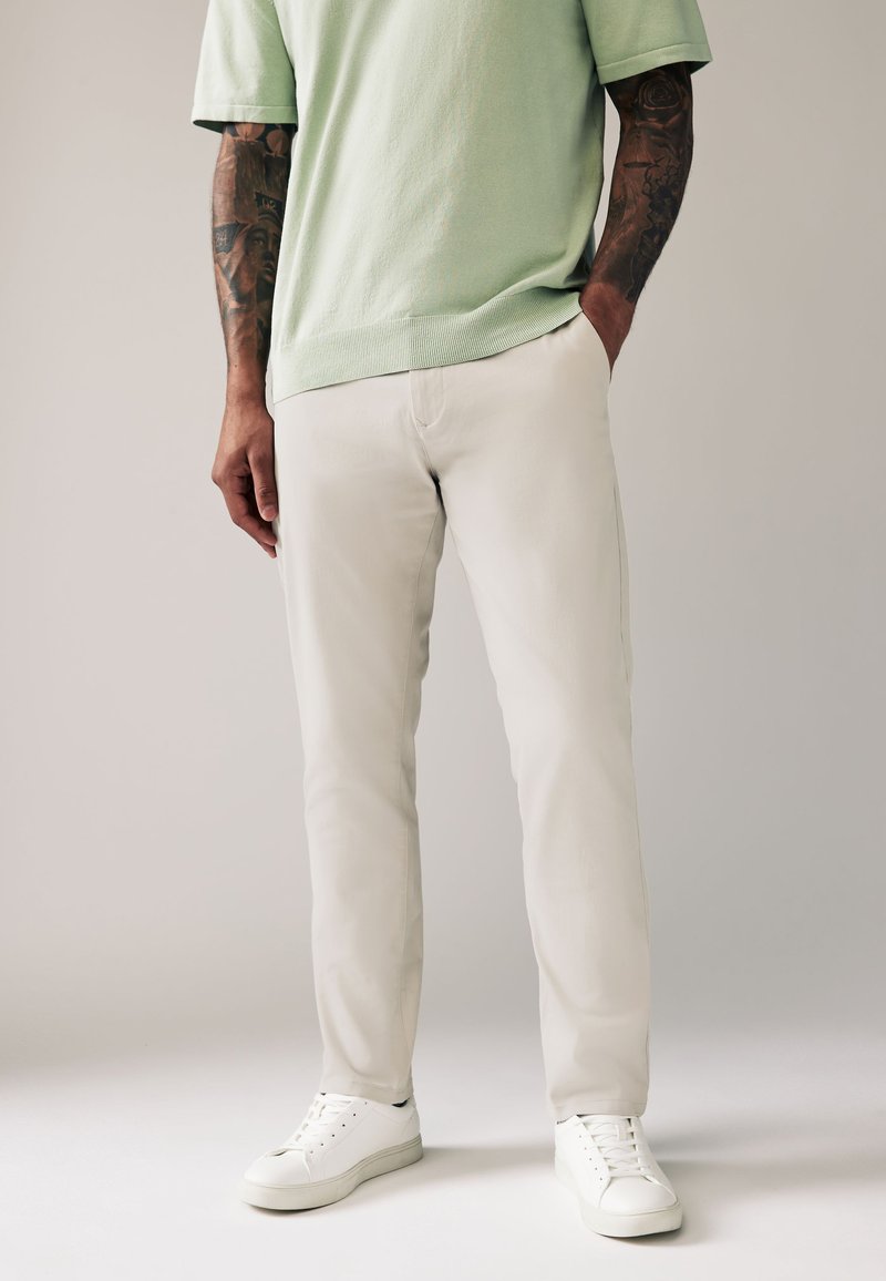 Maglione verde chiaro a maniche corte abbinato a pantaloni su misura color avorio e sneaker bianche, caratterizzato da un tessuto liscio e un design aderente.