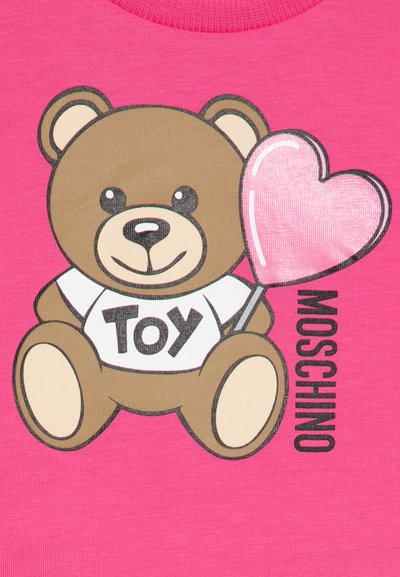 Gráfico de un oso de peluche marrón sobre un fondo rosa, vistiendo una camiseta blanca con "JUGUETE" en negro, sosteniendo un globo de corazón rosa brillante.