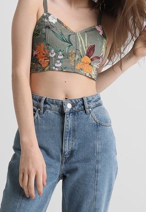Groene bloemencrop top met verstelbare bandjes en geborduurde ontwerpen, gecombineerd met hoge blauwe spijkerbroeken met een knoopsluiting.