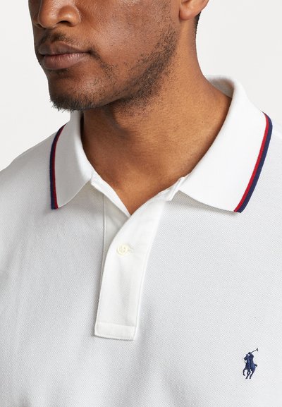 Polo shirt blanche en tissu texturé, avec un col rayé rouge et bleu, une patte de boutonnage à un bouton et un logo marine sur la poitrine.