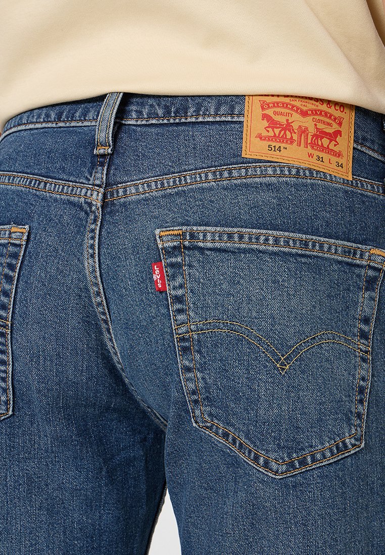 Blå denimjeans med en brun läderetikett vid midjan, gula sömmar och en röd Levi's-tagg på bakfickan. Har en klassisk fickdesign.