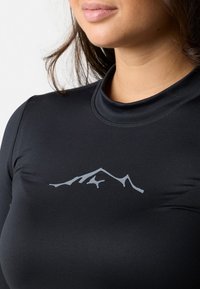 Svart långärmad topp med hög krage och en grå bergslogotyp på bröstet. Tyget ser slätt och figurnära ut.