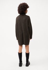 Abito maglione di grandi dimensioni in marrone scuro con colletto alto, tessuto leggermente strutturato e spalle scese, abbinato a stivali neri sopra il ginocchio.