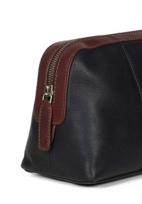 Svart läder toalettväska med brun läderdragkedja och detaljerad sömnad. Har en slät yta och en strukturerad form.