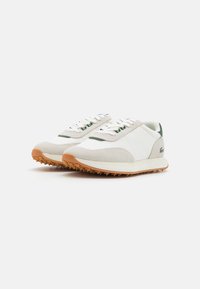 Sneakers bianchi e beige con accenti verdi, suola in gomma e un mix di materiali lisci e testurizzati. Punta tonda con lacci.