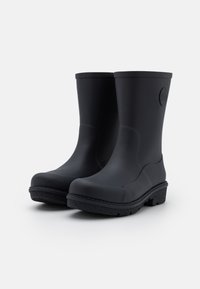 Une paire de bottes en caoutchouc noires mi-mollet avec des semelles texturées et des orteils arrondis sur un fond blanc uni.