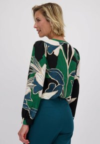 Langarm blouse met een bloemmotief in groen, zwart en roomkleurig, met een ronde hals en elastische manchetten. Soepele textuur en lichtgewicht stof.