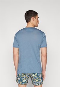 Blue short-sleeve t-shirt made of lightweight fabric, featuring a round neck and a smooth texture, worn with patterned swim shorts.