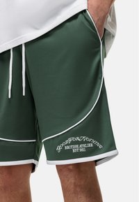 Groene mesh korte broek met witte bies, met een geborduurd logo en tekst op het linkerbeen. Inclusief zijzakken en verstelbare tailleband.