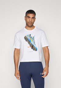T-shirt bianco in cotone con grafica di un scarponcino da calcio blu e giallo, con la scritta "Just Do It", abbinato a pantaloni blu navy.