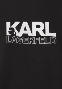 Čierna mikina s výrazným bielym textom "KARL LAGERFELD" a siluetou profilu na ľavej strane.
