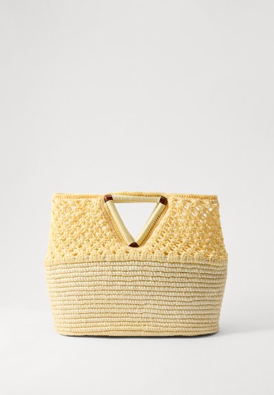Sac en paille tissée jaune avec une poignée en forme de V. Le dessus présente un motif de dentelle délicat, tandis que le bas est lisse et texturé.