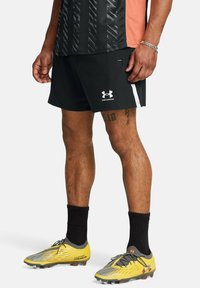 Pantalones cortos deportivos negros con acentos blancos, logo en el dobladillo; botas de fútbol amarillas con detalles grises y tapones rojos; calcetas negras acanaladas.
