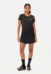 Juodas sijonas-susukimas su lygiu paviršiumi, derinamas su tamsiai pilka aptempta marškinėlių. Dėvimi juodi ir pilki kojinės bei stambūs batai.