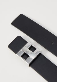 Sort læderbælte med et bredt design, der har en sølvmetalspænde med indgraveringen "HUGO" og et rektangulært udsnit.