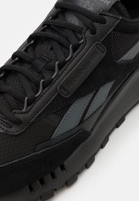 Svart idrottssko med en texturerad tygöversida, mockadetaljer och en tjock gummisula. Inkluderar ton-i-ton snören och logotyp.