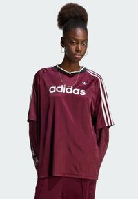 Μακρυμάνικο αθλητικό μπλουζάκι Adidas σε μπορντό χρώμα με λευκό λογότυπο, μαύρο γιακά και τρεις λευκές ρίγες στα μανίκια. Υφασμένο ύφασμα με άνετη εφαρμογή.