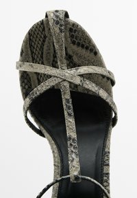 Högklackad sandal med ett orm-mönster i grått och svart. Har tunna remmar och en smal svart sula med en strukturerad finish.