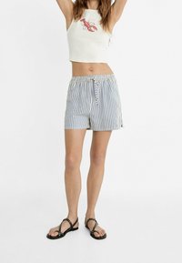 White crop top with red lobster graphic; blue and white striped shorts with elastic waistband and drawstring. Black studded sandals.