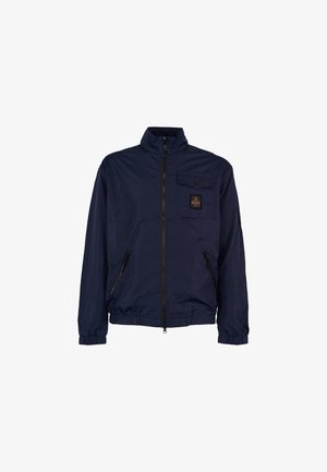 Giacca blu navy realizzata in materiale leggero, con colletto alto, zip frontale, polsini elastici, una tasca sul petto e due tasche laterali con zip.