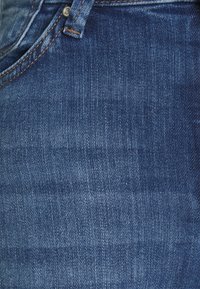 Jeans i denim med en mellanblå tvätt, med en mjuk textur, subtila blekningar, orange sömmar och en silverknapp som stängning.