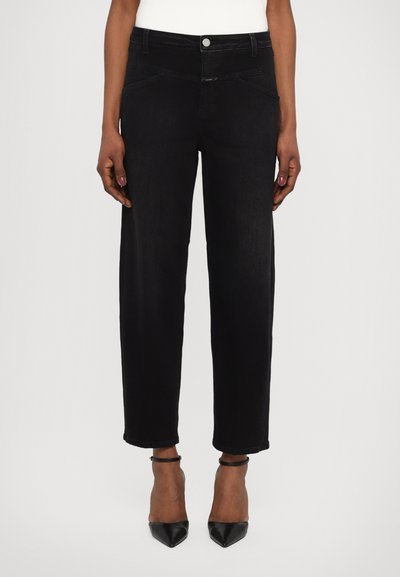 Jean large noir en denim avec taille haute, comportant des poches avant et une fermeture à bouton. Associé à des escarpins noirs à bout pointu.