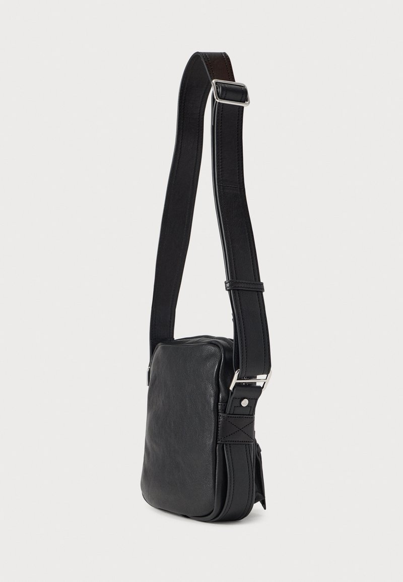 Sort læder skuldertaske med rektangulær form, justerbar strop, sølv beslag og glat tekstur. Har en sidelomme detalje.