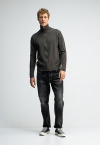 Dunkelgrauer Zip-Up-Pullover mit hohem Kragen, kombiniert mit verwaschenen schwarzen Jeans und schwarzen Sneakern. Der Pullover hat gerippte Bündchen und einen gerippten Saum.