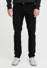 Svarta denimjeans med smal passform, med en klassisk femficksdesign, framknäppning och sömnadsdetaljer. Bärs med grå sneakers.