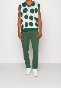 Grön och cremefärgad ärmlös tröja med stora gröna prickar, kombinerad med matchande gröna byxor och vita sneakers.