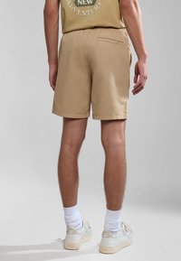 Tan shorts lavet af letvægtsstof med elastisk talje, der har en baglomme og en lige kant, parret med hvide sneakers.