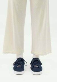 Marineblaue Sneakers aus Stoff mit weißen Gummisohlen und Zunge, kombiniert mit cremefarbenen, weit geschnittenen Hosen und weißen Sneaker-Socken.