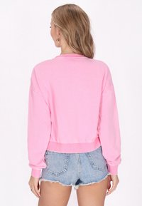 Felpa rosa corta con maniche lunghe, vita a coste e scollatura rotonda, abbinata a pantaloni corti in denim chiaro con orli sfrangiati.