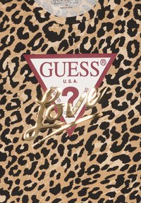 Lapsenes raksts T-krekls no organiskās kokvilnas, ar sarkanu triangulāru emblēmu ar "GUESS" un "U.S.A." uzrakstu, kā arī zelta skripta akcentu "Love".