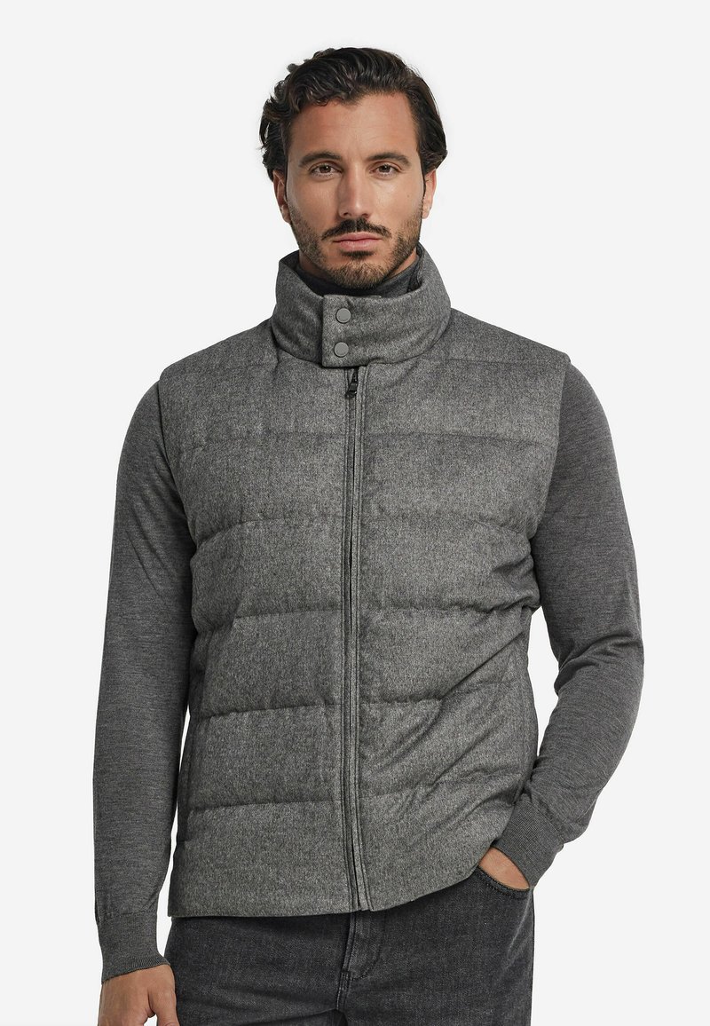 Graue Steppweste mit hohem Kragen, Vorderreißverschluss und Druckknöpfen, getragen über einem langärmligen grauen Oberteil; mit gestepptem Muster.