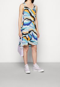 Pestré šaty s vlnitými vzory v modré, žluté a černé barvě. Nosí se s fialovými teniskami a malou levandulovou kabelkou.