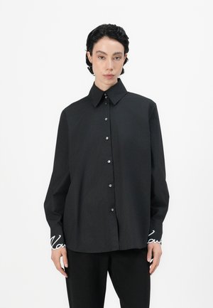Black, long-sleeve shirt with a structured collar, featuring a button-up front and embroidered text on the cuffs. Smooth cotton fabric.