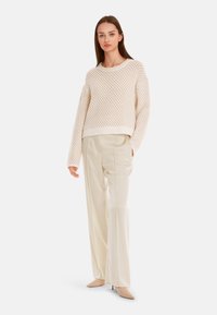 Cream knitted sweater with a textured pattern, paired with high-waisted, wide-leg pale beige trousers and neutral high-heeled shoes.