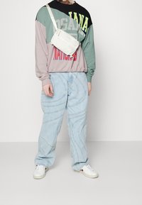 Mikina v několika barvách s grafickým textem, světle modré džíny se zaobleným švem a bílé tenisky. Malá bílá crossbody taška.