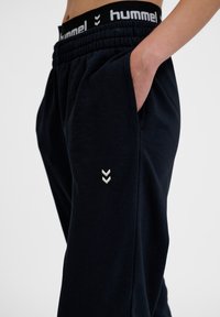 Marineblauwe sweatpants met elastische tailleband, voorzien van een wit logo en chevronontwerp op het onderbeen, gemaakt van zachte stof met zijzakken.