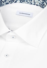 Camicia bianca con finitura strutturata, con colletto interno a motivo floreale e etichetta con la scritta "seidensticker." Chiusura con bottoni.