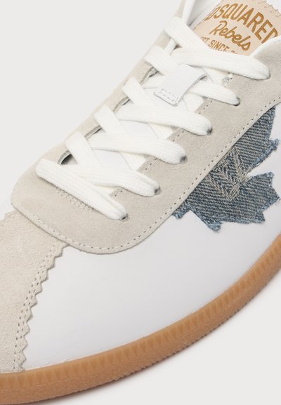 Λευκό και μπεζ sneaker με λευκά κορδόνια, καφέ σόλα, τζιν έμπλαστρο φύλλου σφενδάμου στο πλάι και μερικώς χρυσό λογότυπο "Dsquared2" στη γλώσσα.