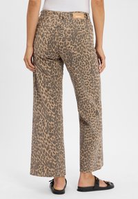 Jean large à imprimé léopard en beige et marron avec poches arrière et emblème en cuir. Associé à des sandales plates noires.