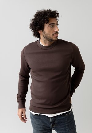 Dark brown crewneck sweatshirt with long sleeves, smooth texture, and a fitted design, paired with a white undershirt and blue jeans.